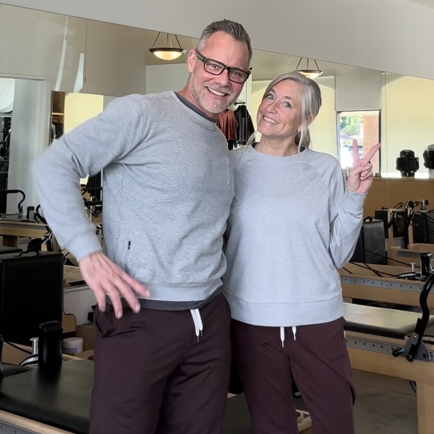 Sean and Michele and are both wearing gray T-shirts and burgundy pants while in the pilates studio